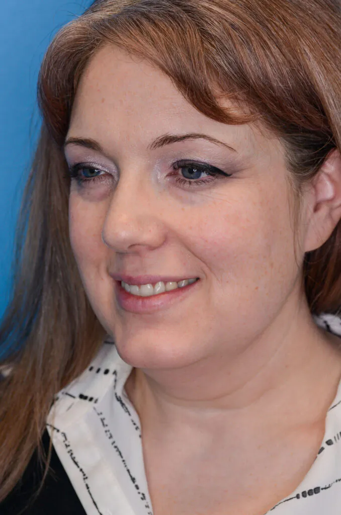 Woman smiles while looking to the side against blue background.